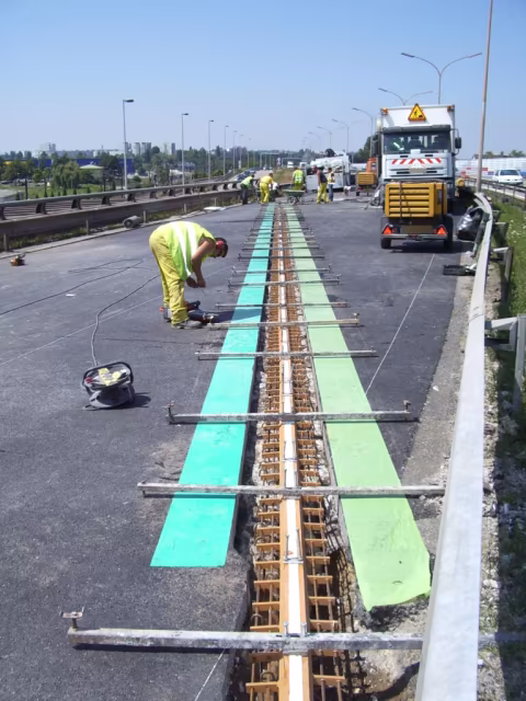 Ouvriers posant un joint de dilatation sur un pont routier avec équipements de chantier.