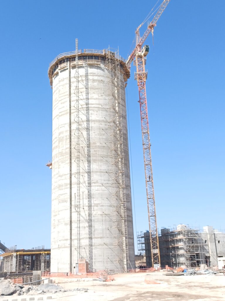 Silo en béton en cours de construction avec échafaudages et grue sur site industriel.